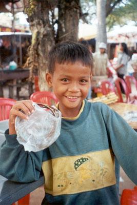 A young boy helps his mother sell souvenirs at an outdoor stand near Angkor Wat