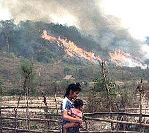A young woman with a baby in the fields as vegetation is burnt off in the background, at a Hmong village resettled in the Xiengkhone district of the northern Laos province of Xayaburi.
