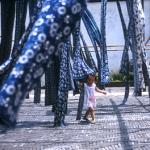 A young girl plays in the skeins of traditional blue and white tie-died fabric as they dry in a courtyard.